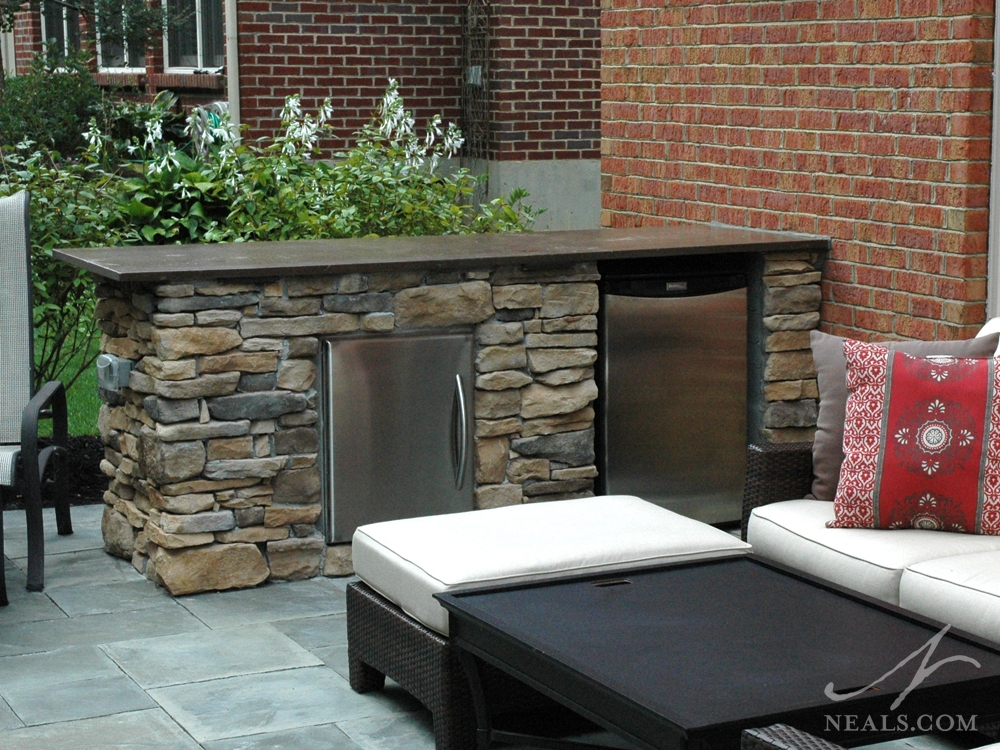 A short retaining wall near a sitting area in this backyard patio offers the perfect spot for a beverage refrigerator. A stainless steel cabinet offers additional weather-safe storage.