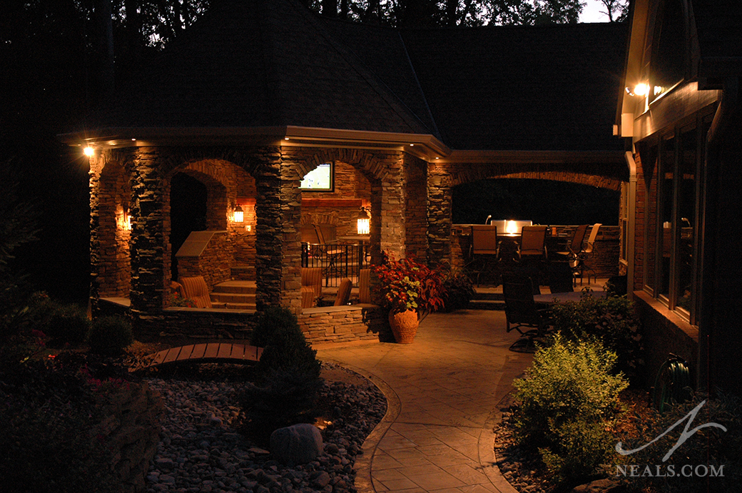 In the evening, lighting added to all areas of this backyard pavilion helps to highlight the walkway and illuminate the interior, but also illuminates the landscape.